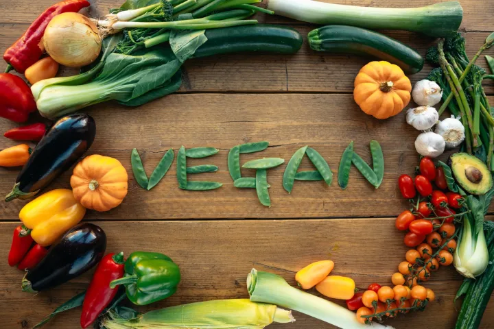 Top view of fresh vegetables forming the word 'VEGAN' on a rustic wooden surface.