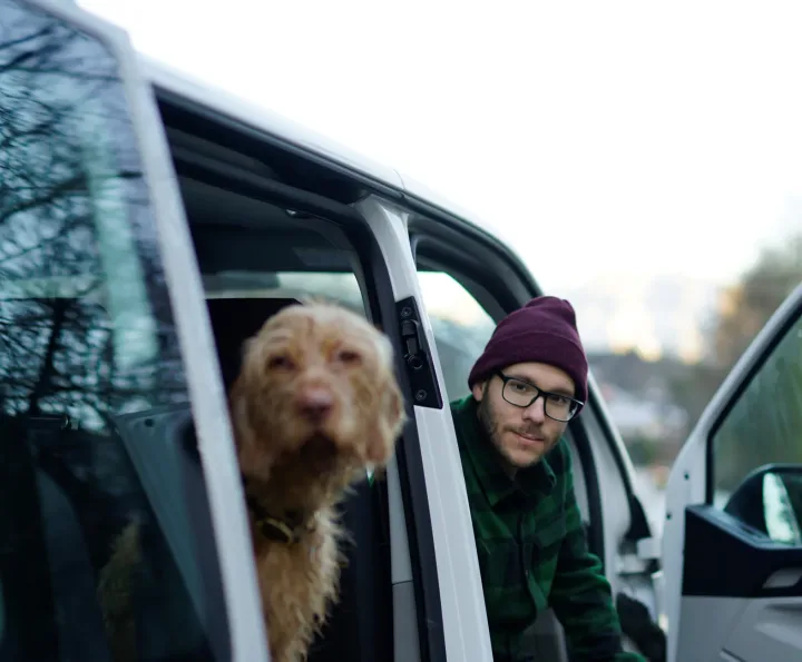 A man with a dog in a van outdoors, creating a scene of friendship and travel.